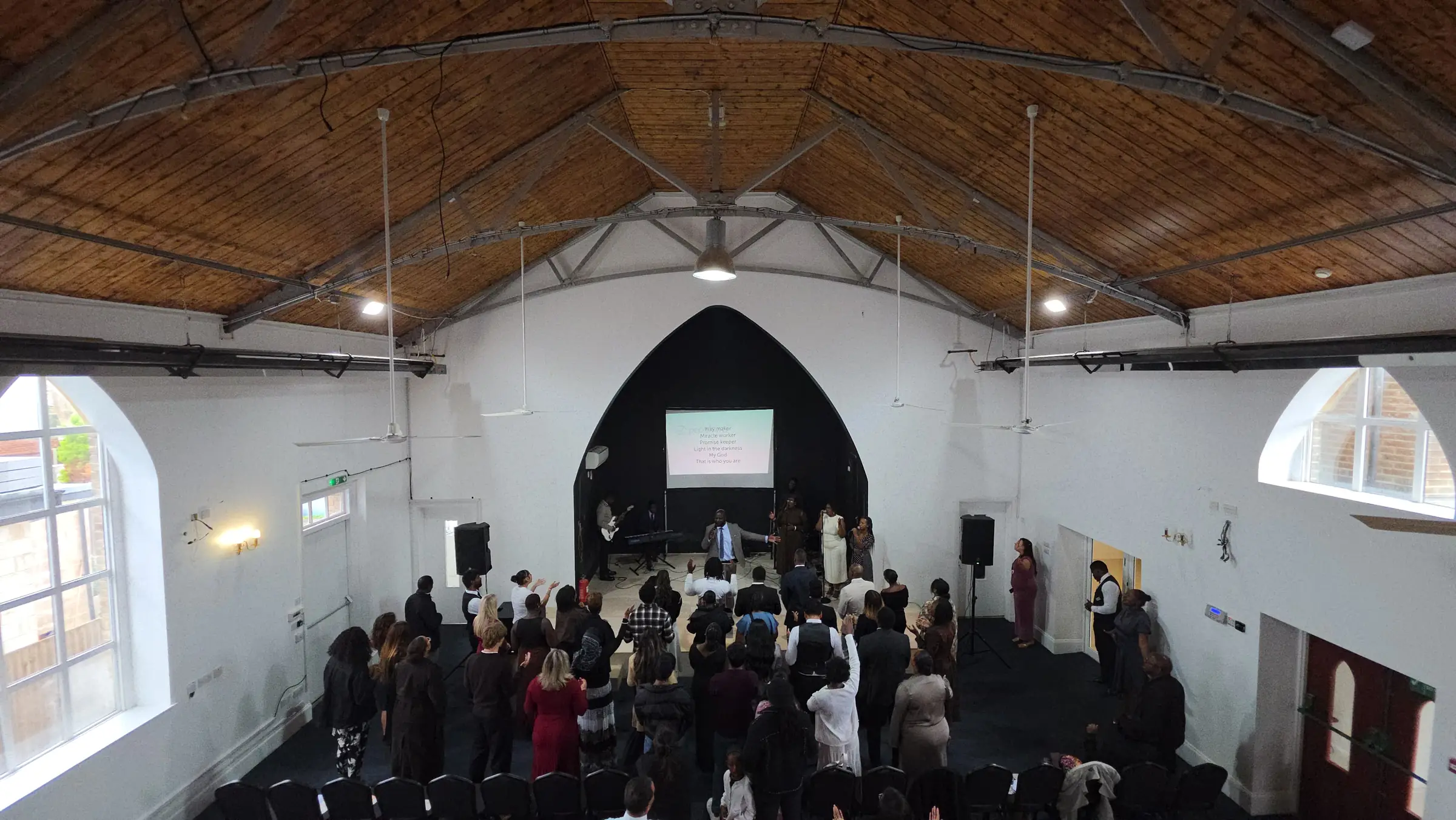 The congregation worshipping in the main hall at 80–96 Cambridge Road, under a timber roof and a tall pointed arch